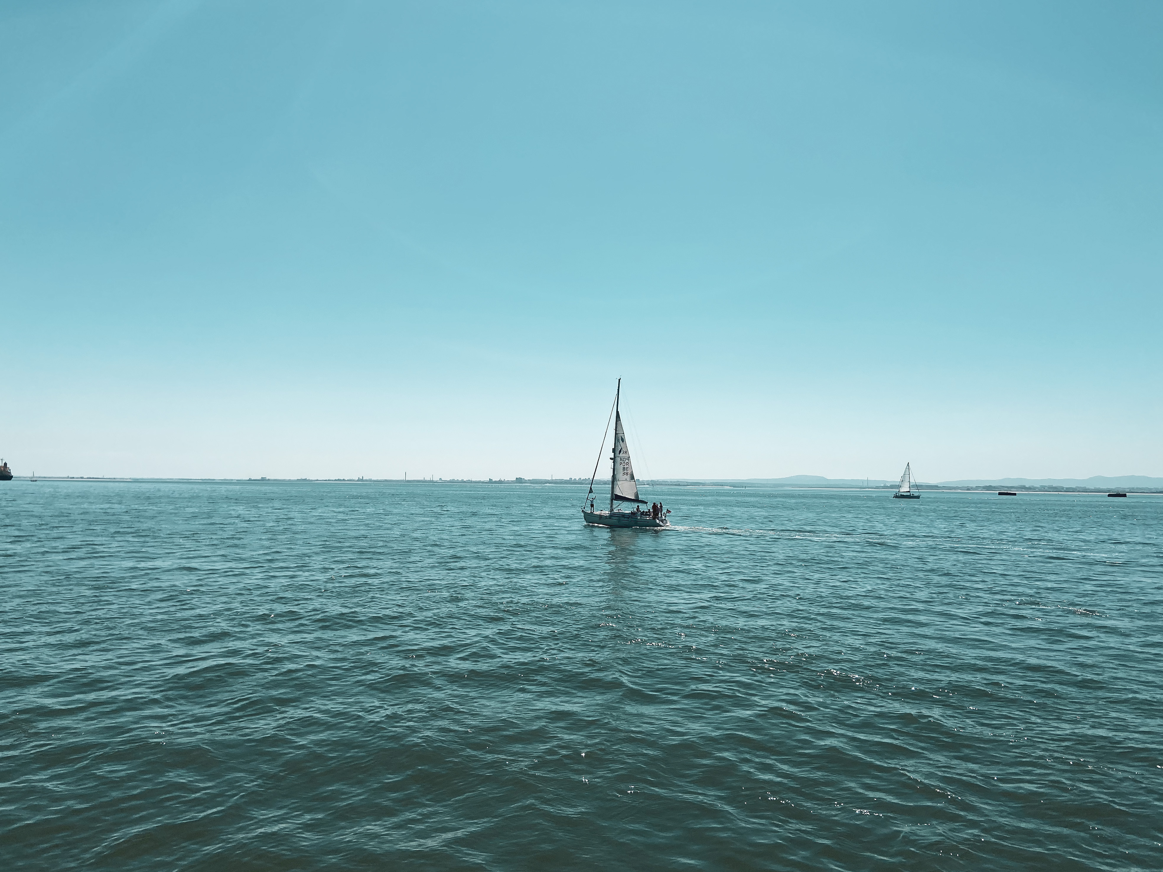 Travel during COVID 19. A sailboat sails across the harbour in Lisbon under a clear blue sky.